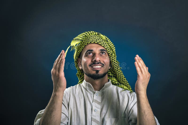 Oriental-looking man in traditional Arab national dress smiles happily, raising his eyes and hands to heaven