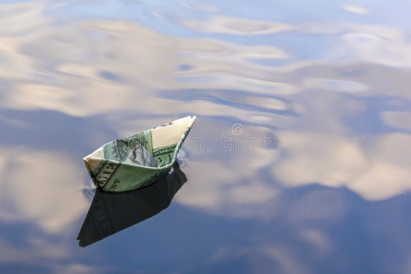 Origami boat built of one hundred dollar bill. paper boat from a hundred dollar bill in blue water. copy space. Concept: stock images Origami boat built of one hundred dollar bill. paper boat from a hundred dollar bill in blue water. copy space. Concept: stock images