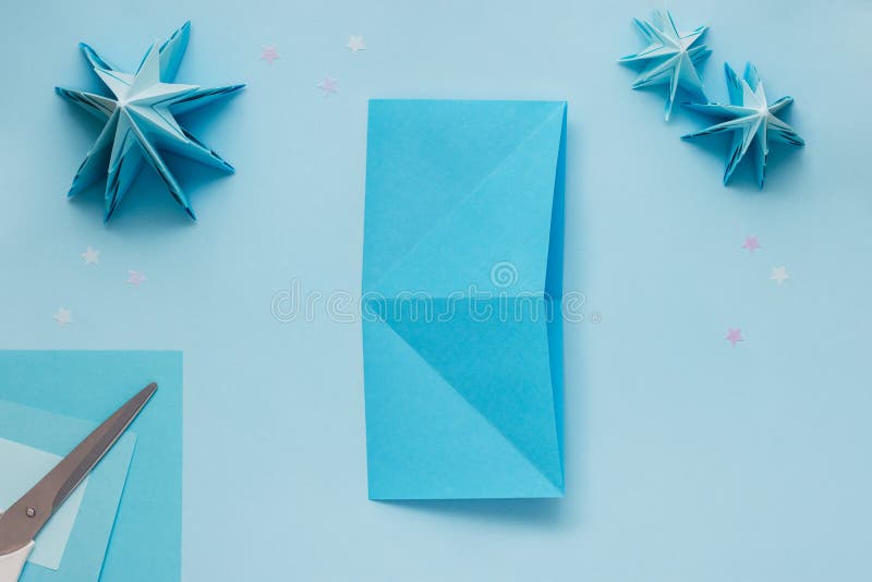 Simple origami 3D Christmas tree made from blue paper. Step by step instruction, step 5. Unfold the sheet rotate 90 degrees and fold again. Simple origami 3D Christmas tree made from blue paper. Step by step instruction, step 5. Unfold the sheet rotate 90 degrees and fold again