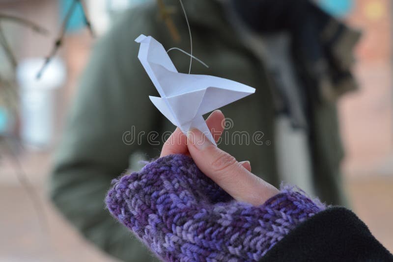 Origami volanti dell'uccello della carta tenuti da una mano della donna in primo piano di inverno immagine stock Origami volanti dell'uccello della carta tenuti da una mano della donna in primo piano di inverno immagine stock