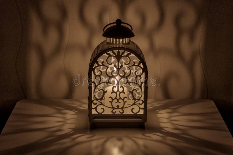 Ornamental lantern with burning candle. Decorative shadows. Festive table composition at night. royalty free stock photography