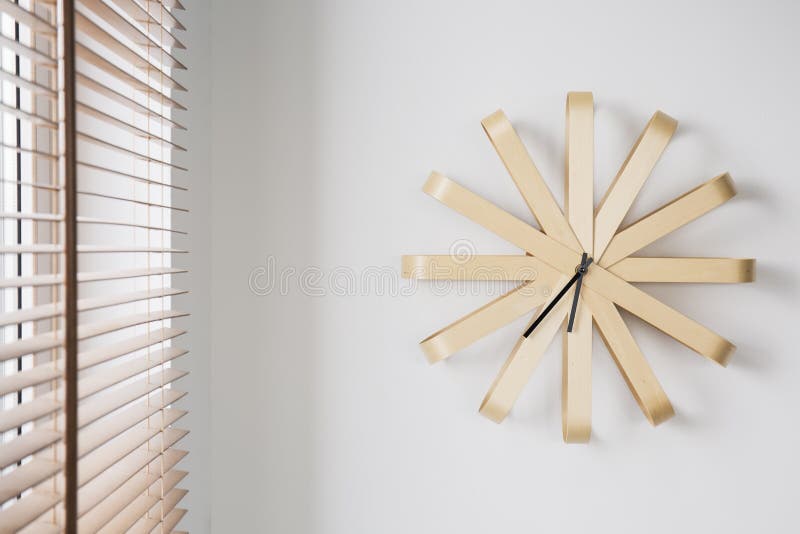 Orologio di legno moderno sulla parete bianca accanto alla finestra con i ciechi nell'interno piano semplice Foto reale fotografia stock libera da diritti Orologio di legno moderno sulla parete bianca accanto alla finestra con i ciechi nell'interno piano semplice Foto reale fotografia stock libera da diritti