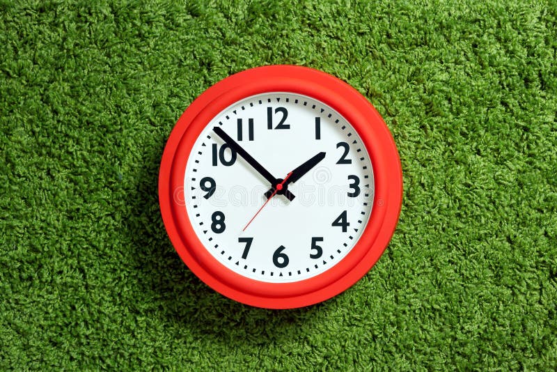 Orologio rosso con il quadrante bianco sul tappeto verde. Orologio rosso con il quadrante bianco che mette sul tappeto verde del vello, scena astratta di tempo