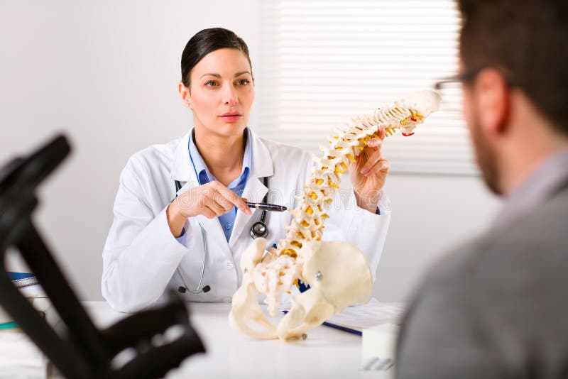 Female Orthopaedic surgeon explaining a back injury or disease to a male patient on crutches with the help of a human spine. Female Orthopaedic surgeon explaining a back injury or disease to a male patient on crutches with the help of a human spine