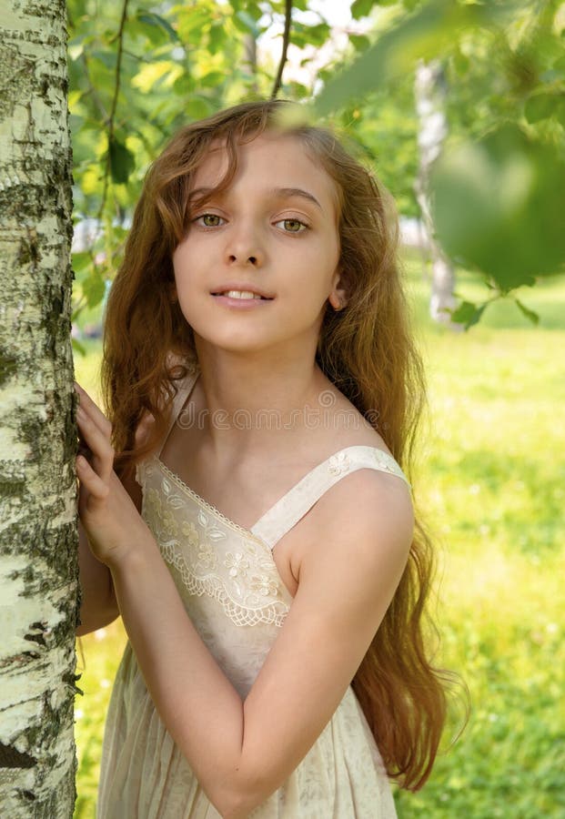 Beautiful white girl 11 years old with long hair standing near a birch tree...