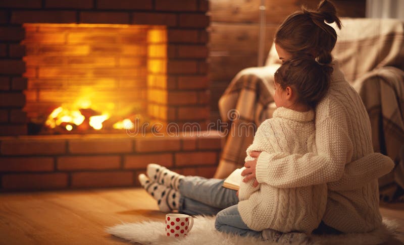 Os abraços da mãe e da criança da família e aquecem-se na noite do inverno pelo firep