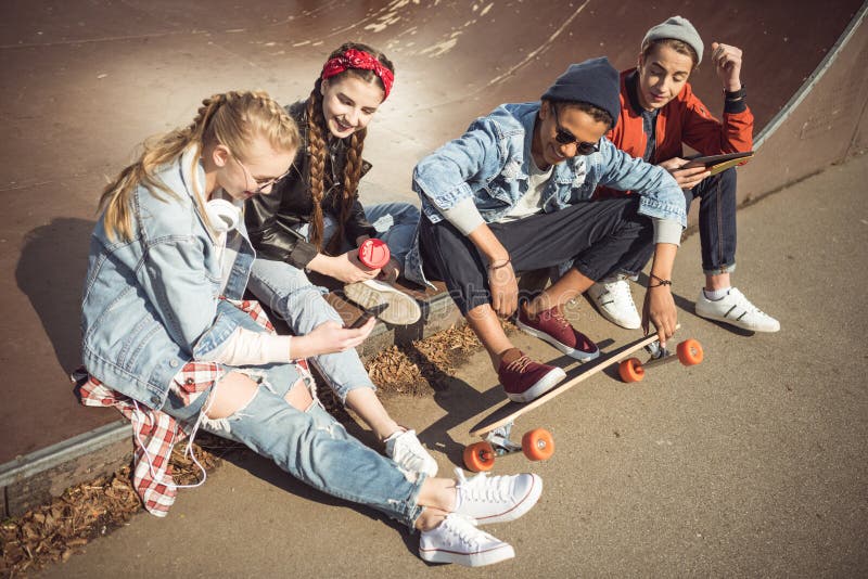 Os adolescentes agrupam o assento de assento junto e a utilização de dispositivos digitais fotografia de stock Os adolescentes agrupam o assento de assento junto e a utilização de dispositivos digitais fotografia de stock