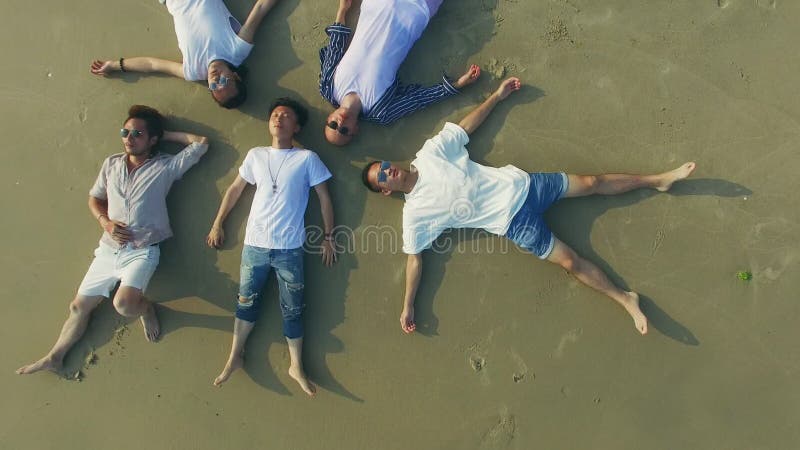 Os adultos asiáticos novos que encontram-se sobre suportam nos olhos da praia da areia fechados