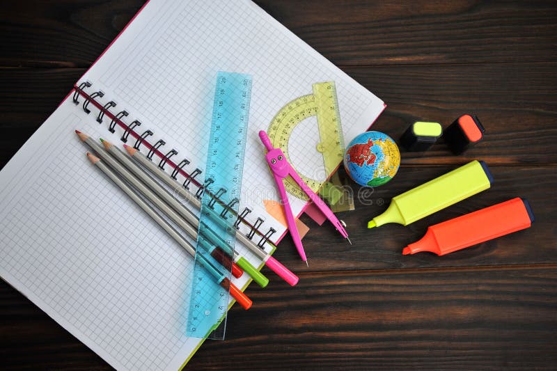 Os artigos de papelaria dispersaram em um caderno que encontra-se em uma tabela de madeira escura, imagem de stock Os artigos de papelaria dispersaram em um caderno que encontra-se em uma tabela de madeira escura, imagem de stock