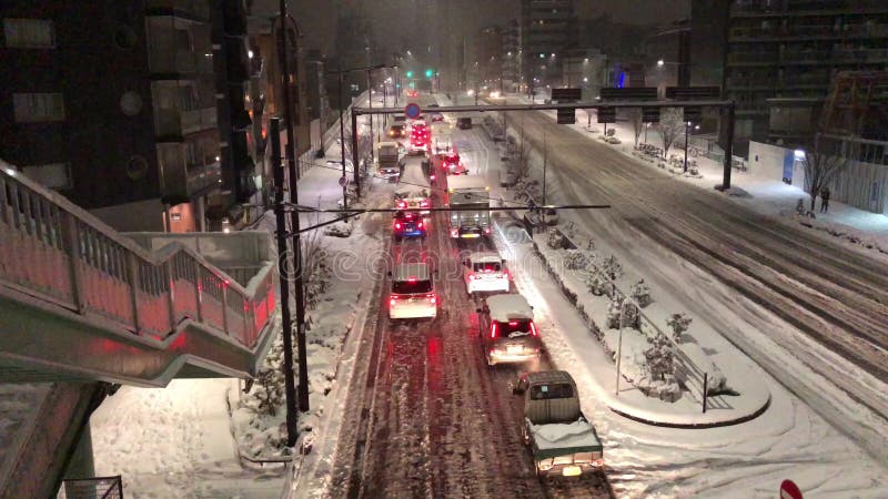 Os carros colados no Tóquio como pedestres e o tráfego esforçam-se durante uma tempestade rara da neve