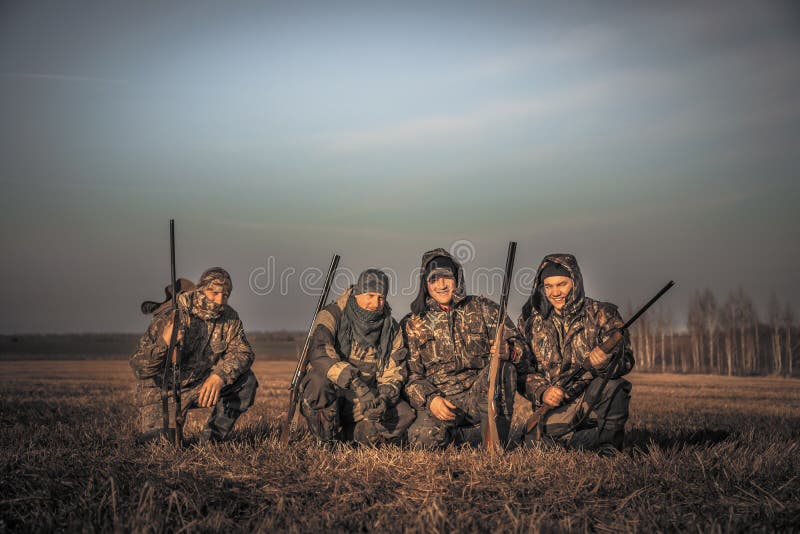 Os caçadores dos homens agrupam o retrato da equipe no campo rural que levanta junto contra o céu do nascer do sol durante a époc fotos de stock royalty free Os caçadores dos homens agrupam o retrato da equipe no campo rural que levanta junto contra o céu do nascer do sol durante a époc fotos de stock royalty free