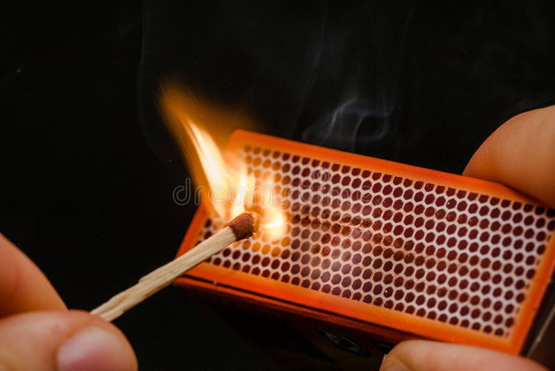 Man's fingers lighting a match, rubbing against the matchbox, setting fire to friction. On a black background. Matches and fire. Man's fingers lighting a match, rubbing against the matchbox, setting fire to friction. On a black background. Matches and fire