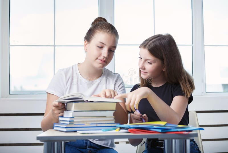 Os estudantes dos adolescentes dos adolescentes estão sentando-se na tabela com st dos livros imagens de stock royalty free Os estudantes dos adolescentes dos adolescentes estão sentando-se na tabela com st dos livros imagens de stock royalty free