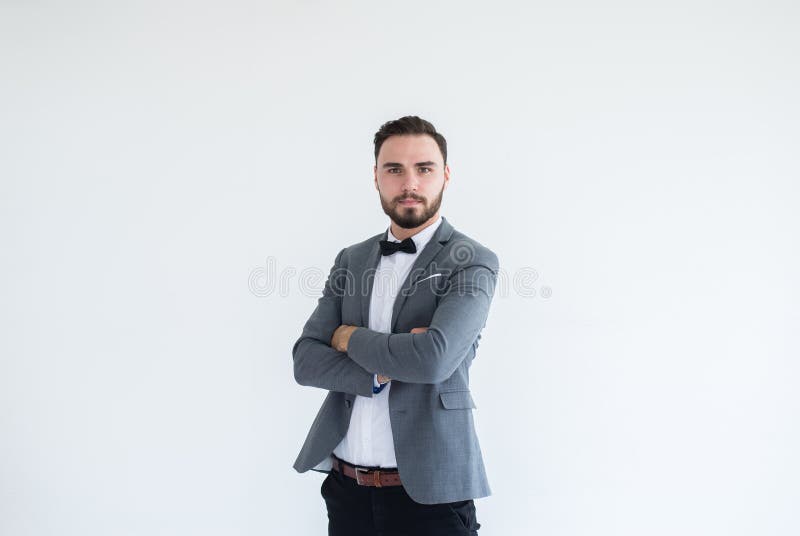 Os homens caucasianos consideráveis com a barba na posição formal do smoking e do terno e os braços transversais no fundo branco, imagens de stock Os homens caucasianos consideráveis com a barba na posição formal do smoking e do terno e os braços transversais no fundo branco, imagens de stock