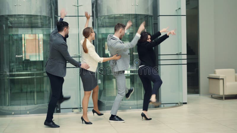 Os homens e os empresários de riso das mulheres estão tendo o divertimento na dança do partido de escritório na entrada que aprec