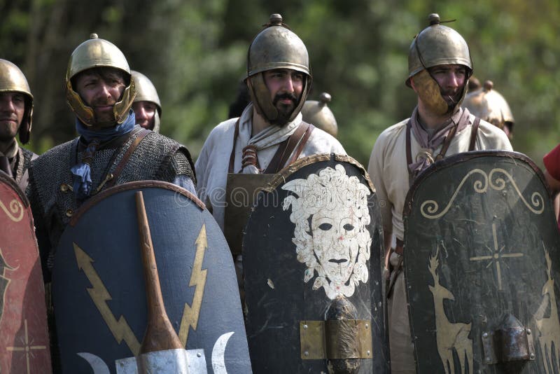 Os legionários romanos que vestem capacetes e protetores olham sobre na formação da defesa imagens de stock Os legionários romanos que vestem capacetes e protetores olham sobre na formação da defesa imagens de stock