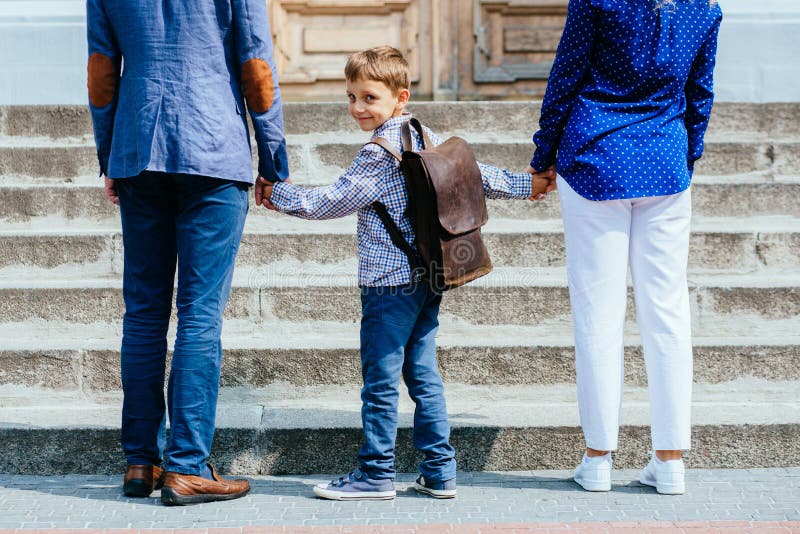 Os pais irreconhecíveis tomam a criança à escola O aluno da escola primária vai estudo com trouxa Opinião traseira o pai, mãe fotos de stock royalty free Os pais irreconhecíveis tomam a criança à escola O aluno da escola primária vai estudo com trouxa Opinião traseira o pai, mãe fotos de stock royalty free