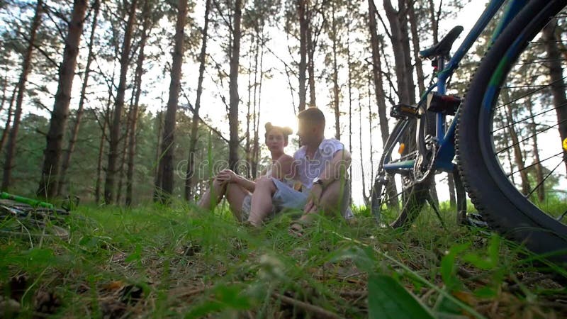 Os pares caucasianos novos têm um resto na grama após a ciclagem através da floresta