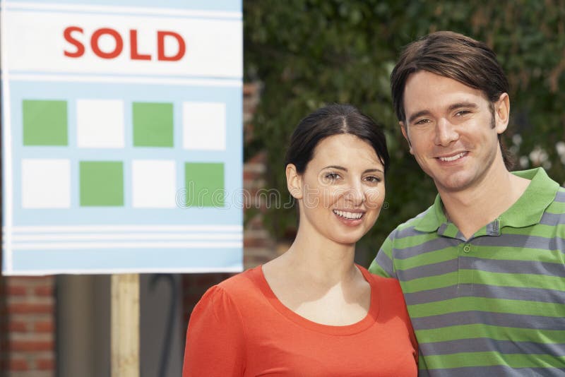Os pares em Front Of New Home With venderam o sinal imagens de stock Os pares em Front Of New Home With venderam o sinal imagens de stock