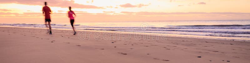 Os pares estão correndo na praia no nascer do sol foto de stock royalty free Os pares estão correndo na praia no nascer do sol foto de stock royalty free