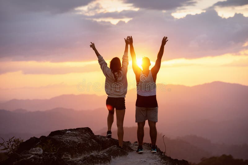 Os pares felizes levantaram a parte superior da montanha do armssunset foto de stock royalty free Os pares felizes levantaram a parte superior da montanha do armssunset foto de stock royalty free