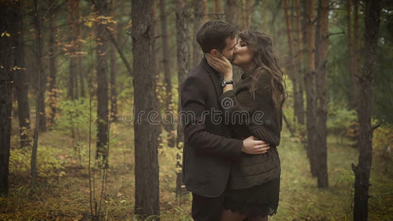 Os pares felizes que têm uma data no homem e na mulher de sorriso da floresta estão estando entre as árvores e estão abraçando-se
