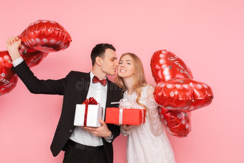 Os pares no amor, em um homem e em uma mulher dão-se presentes, caixas de presente da posse e balões, no estúdio em um fundo cor- imagem de stock Os pares no amor, em um homem e em uma mulher dão-se presentes, caixas de presente da posse e balões, no estúdio em um fundo cor- imagem de stock