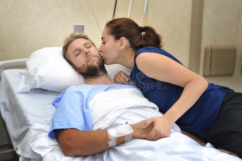 Os pares novos na sala de hospital equipam o encontro na mulher preocupada cama que guarda seu inquietação da mão fotos de stock Os pares novos na sala de hospital equipam o encontro na mulher preocupada cama que guarda seu inquietação da mão fotos de stock