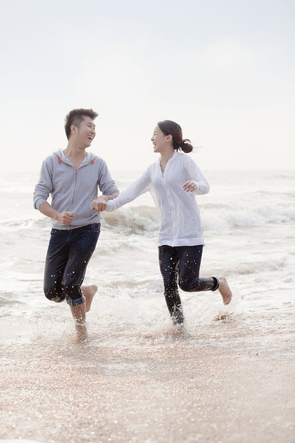 Os pares novos que guardaram as mãos e o corredor pelas águas afiam na praia, China fotos de stock Os pares novos que guardaram as mãos e o corredor pelas águas afiam na praia, China fotos de stock