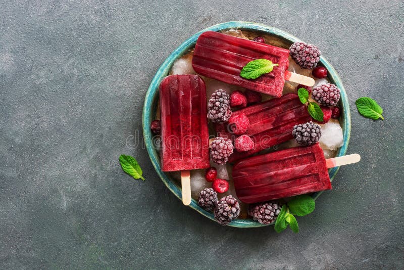 Os picolés caseiros do gelado da amora-preta das framboesas decoraram bagas e folhas de hortelã na placa com os cubos de gelo no imagens de stock Os picolés caseiros do gelado da amora-preta das framboesas decoraram bagas e folhas de hortelã na placa com os cubos de gelo no imagens de stock