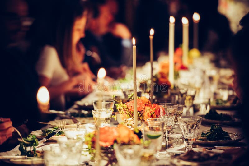 Os povos apreciam um jantar da família com velas Tabela grande servida com alimento e bebidas foto de stock Os povos apreciam um jantar da família com velas Tabela grande servida com alimento e bebidas foto de stock