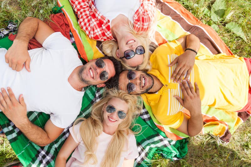 Os povos felizes agrupam os amigos novos que encontram-se para baixo na cobertura do piquenique exterior imagem de stock Os povos felizes agrupam os amigos novos que encontram-se para baixo na cobertura do piquenique exterior imagem de stock