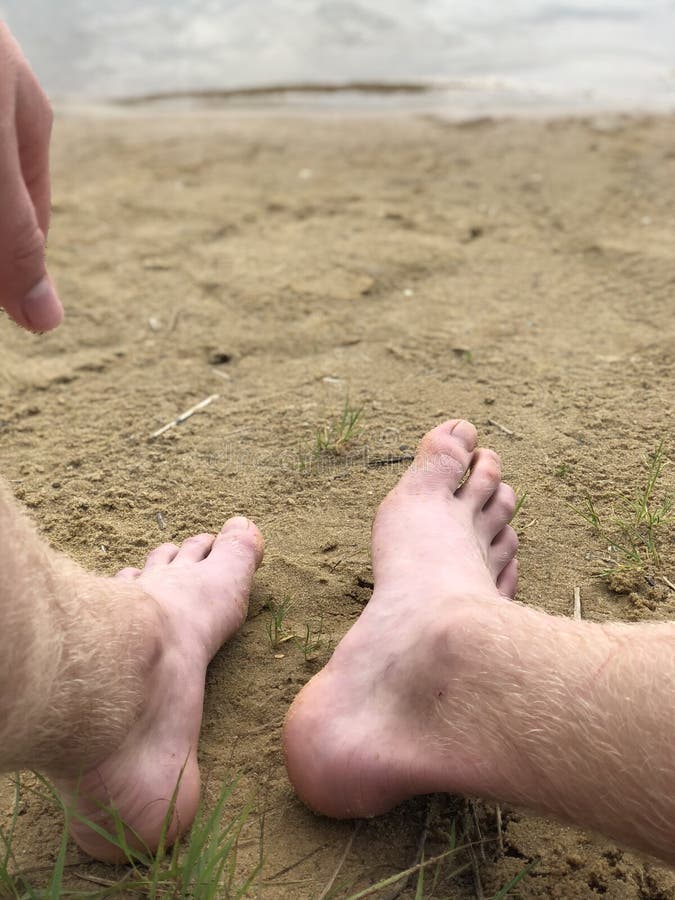 Os pés e a mão dos homens contra a areia e o rio fotografia de stock Os pés e a mão dos homens contra a areia e o rio fotografia de stock