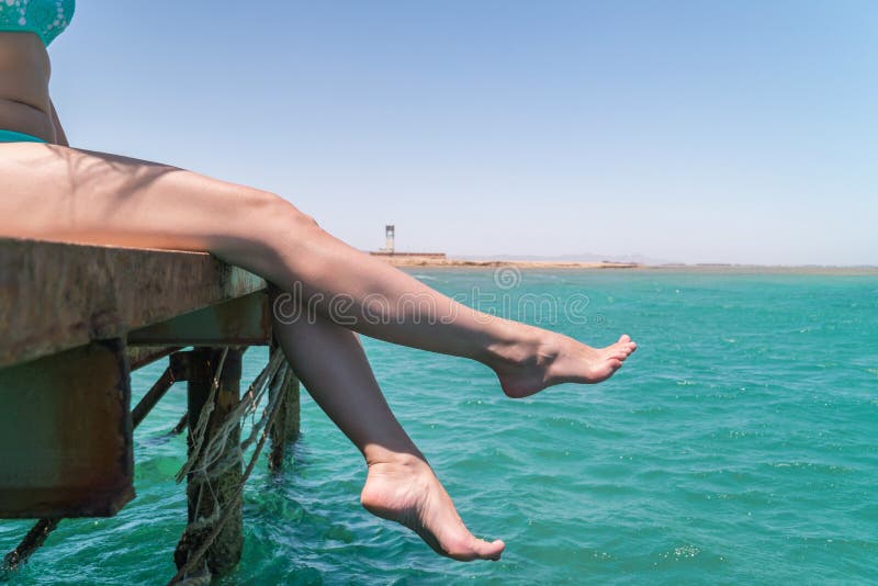 Os pés fêmeas novos penduram do cais sobre a água do mar fotografia de stock Os pés fêmeas novos penduram do cais sobre a água do mar fotografia de stock