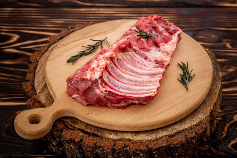 Os reforços de carne de porco cortados crus na placa servindo de madeira, fecham-se acima no fundo de madeira Conceito do aliment imagem de stock Os reforços de carne de porco cortados crus na placa servindo de madeira, fecham-se acima no fundo de madeira Conceito do aliment imagem de stock