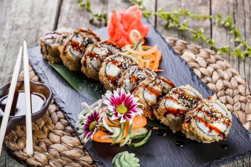 Os rolos de sushi e o maki fritados quentes ajustaram-se com enguia fumado, queijo creme, abacate e wasabi na pedra preta na este fotografia de stock Os rolos de sushi e o maki fritados quentes ajustaram-se com enguia fumado, queijo creme, abacate e wasabi na pedra preta na este fotografia de stock