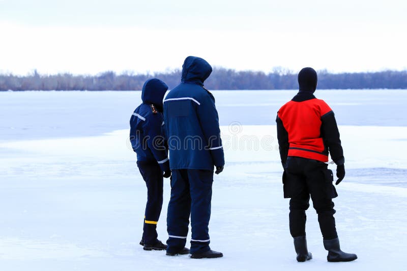 Os salvadores no uniforme e no terno de mergulho estão no dever no rio congelado durante a pesca e os eventos desportivos do inve imagens de stock Os salvadores no uniforme e no terno de mergulho estão no dever no rio congelado durante a pesca e os eventos desportivos do inve imagens de stock