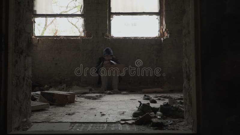 Os sem abrigo com fome congelados com ajuda da placa sentam-se na construção abandonada