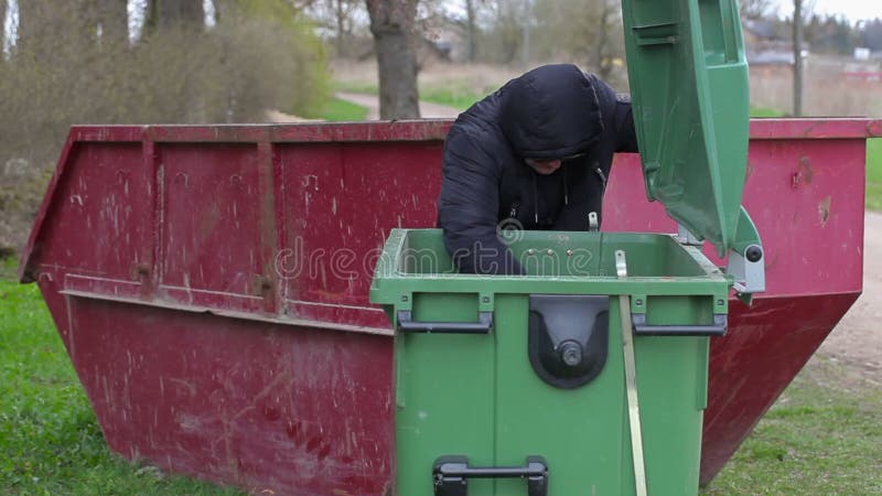 Os sem abrigo tentam encontrar o alimento no recipiente waste