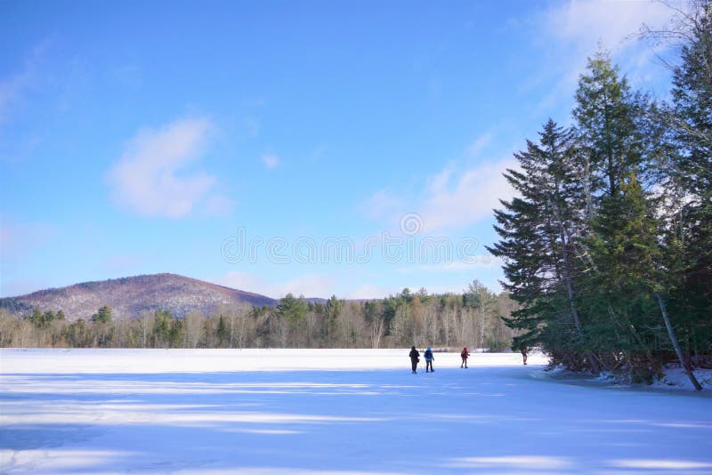 Os snowshoers distantes cruzam o lago congelado no dia de inverno ensolarado foto de stock royalty free Os snowshoers distantes cruzam o lago congelado no dia de inverno ensolarado foto de stock royalty free