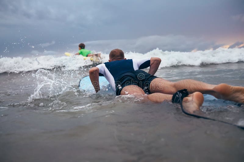 Os surfistas do pai e do filho superam ondas na linha da ressaca foto de stock Os surfistas do pai e do filho superam ondas na linha da ressaca foto de stock