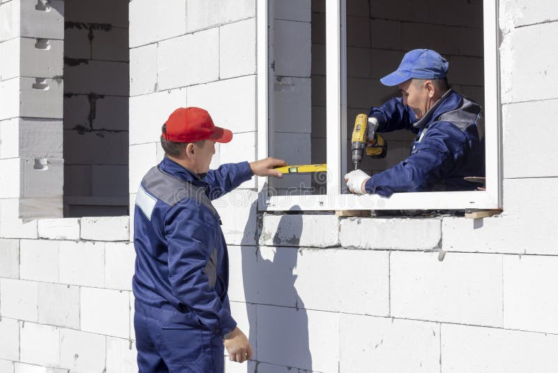 Os trabalhadores instalam a vitrificação em uma casa sob a construção foto de stock Os trabalhadores instalam a vitrificação em uma casa sob a construção foto de stock