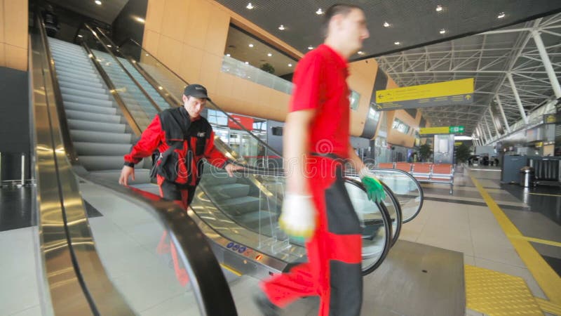 Os trabalhadores no vermelho vão abaixo da escada rolante no salão do aeroporto