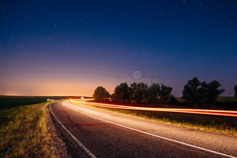 Os traços dos faróis do carro em uma noite ajardinam com um unde da estrada fotos de stock royalty free Os traços dos faróis do carro em uma noite ajardinam com um unde da estrada fotos de stock royalty free