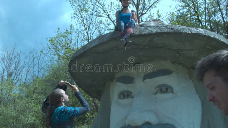 Os turistas são fotografados no monumento a uma cabeça grande em um chapéu Uma moça em um capacete senta-se no chapéu do ` s do m