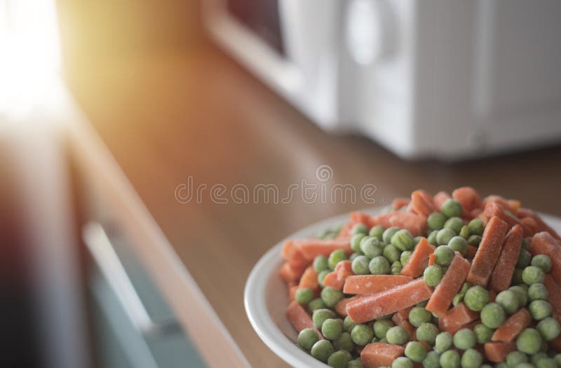 Os vegetais congelados no branco plat perto da micro-ondas na cozinha, cooki
