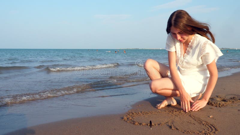 Osamotniona nastoletnia dziewczyna rysuje serce w piasku