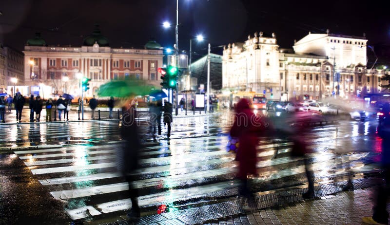 Oskarpt folk som korsar stadsgatan i regnig natt royaltyfri bild Oskarpt folk som korsar stadsgatan i regnig natt royaltyfri bild