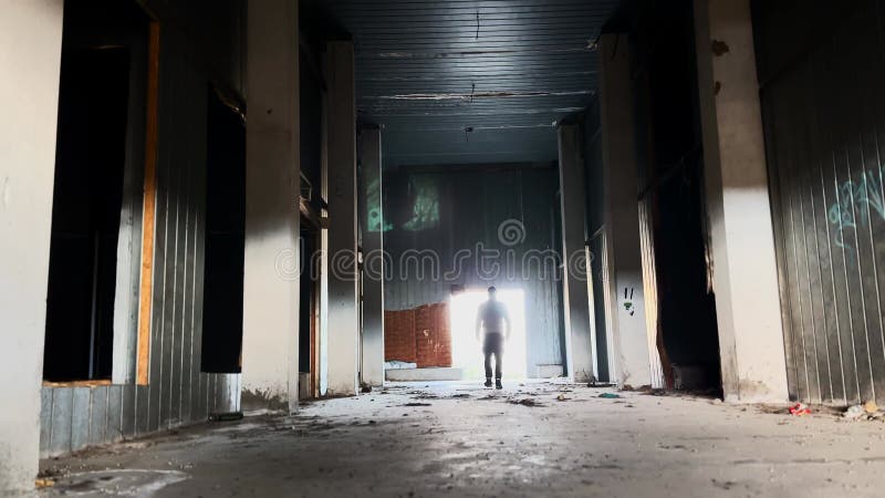 Osoba chodząca w kierunku wyjścia z opuszczonej fabryki