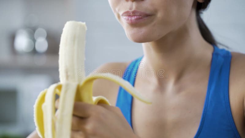 Ostenta a mulher com prazer que come a banana doce, com fome após o exercício ativo